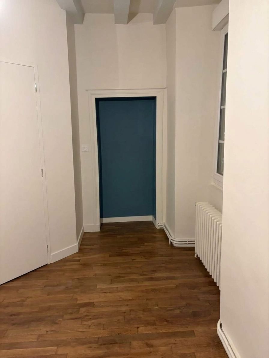 Couloir étroit avec un parquet, des murs blancs et une porte bleue au fond
