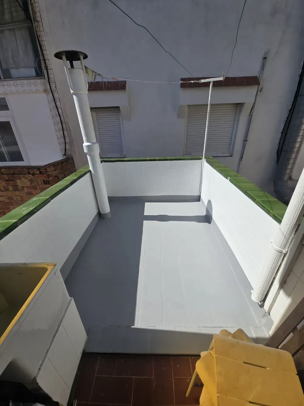 Pequeña terraza en la azotea con paredes blancas, suelo gris y chimenea.