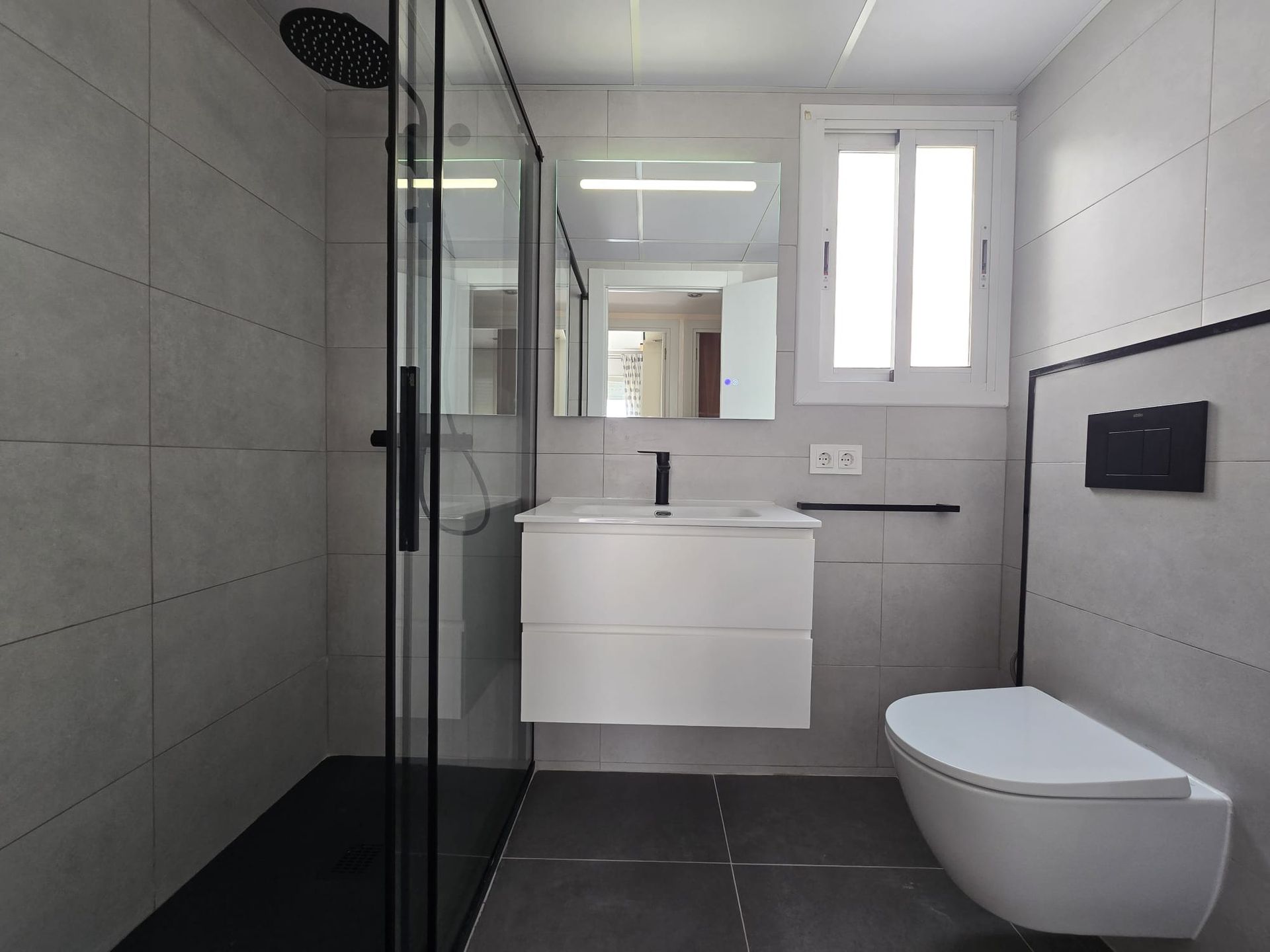 Baño moderno con ducha de cristal, tocador flotante e inodoro montado en la pared.