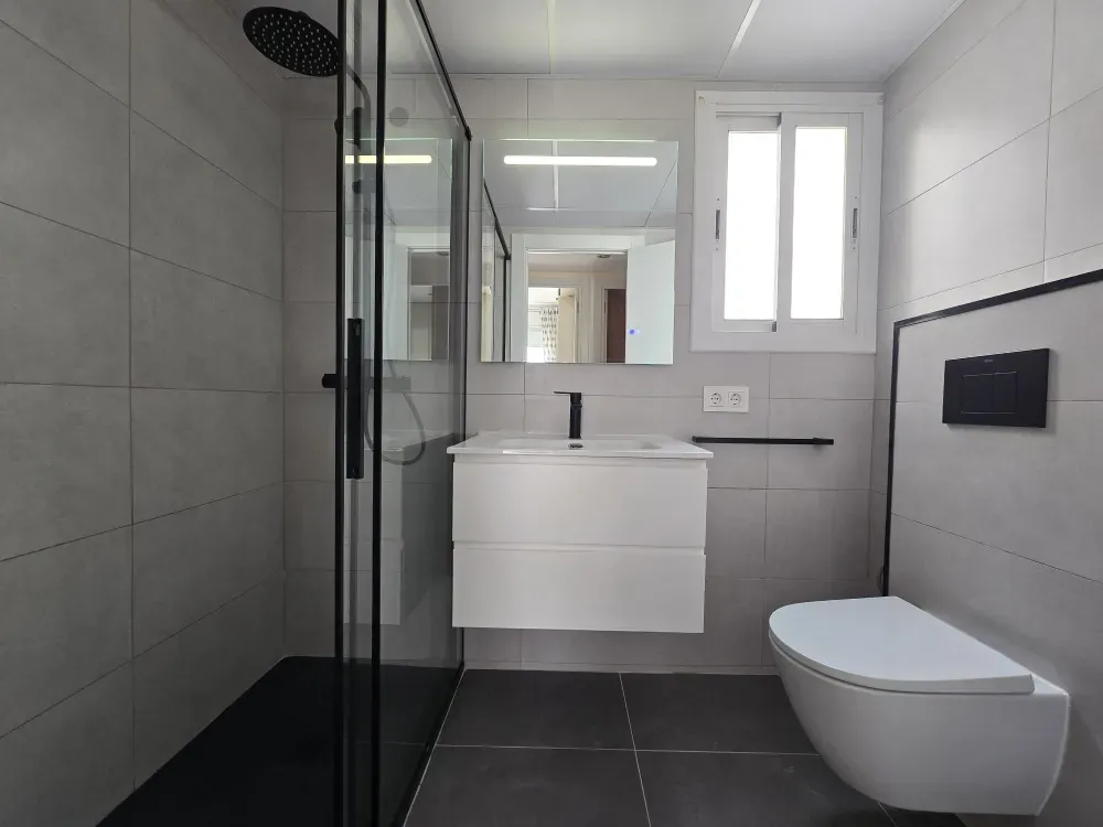 Baño moderno con ducha de cristal, tocador flotante e inodoro montado en la pared.