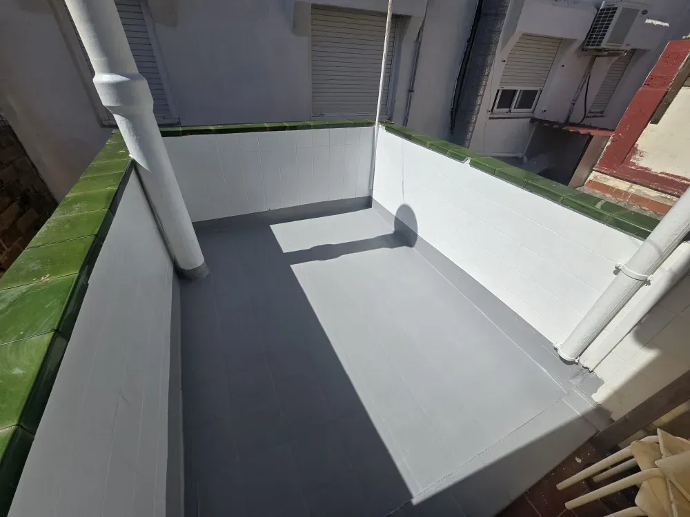 Pequeño balcón con piso gris, paredes blancas y molduras verdes.