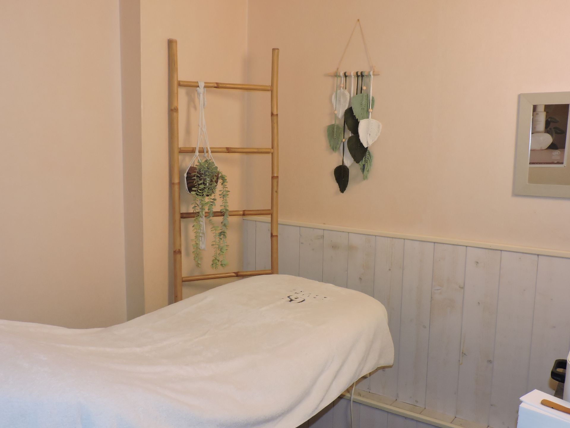 Salle de soins spa avec table de massage, échelle en bambou et décoration murale.