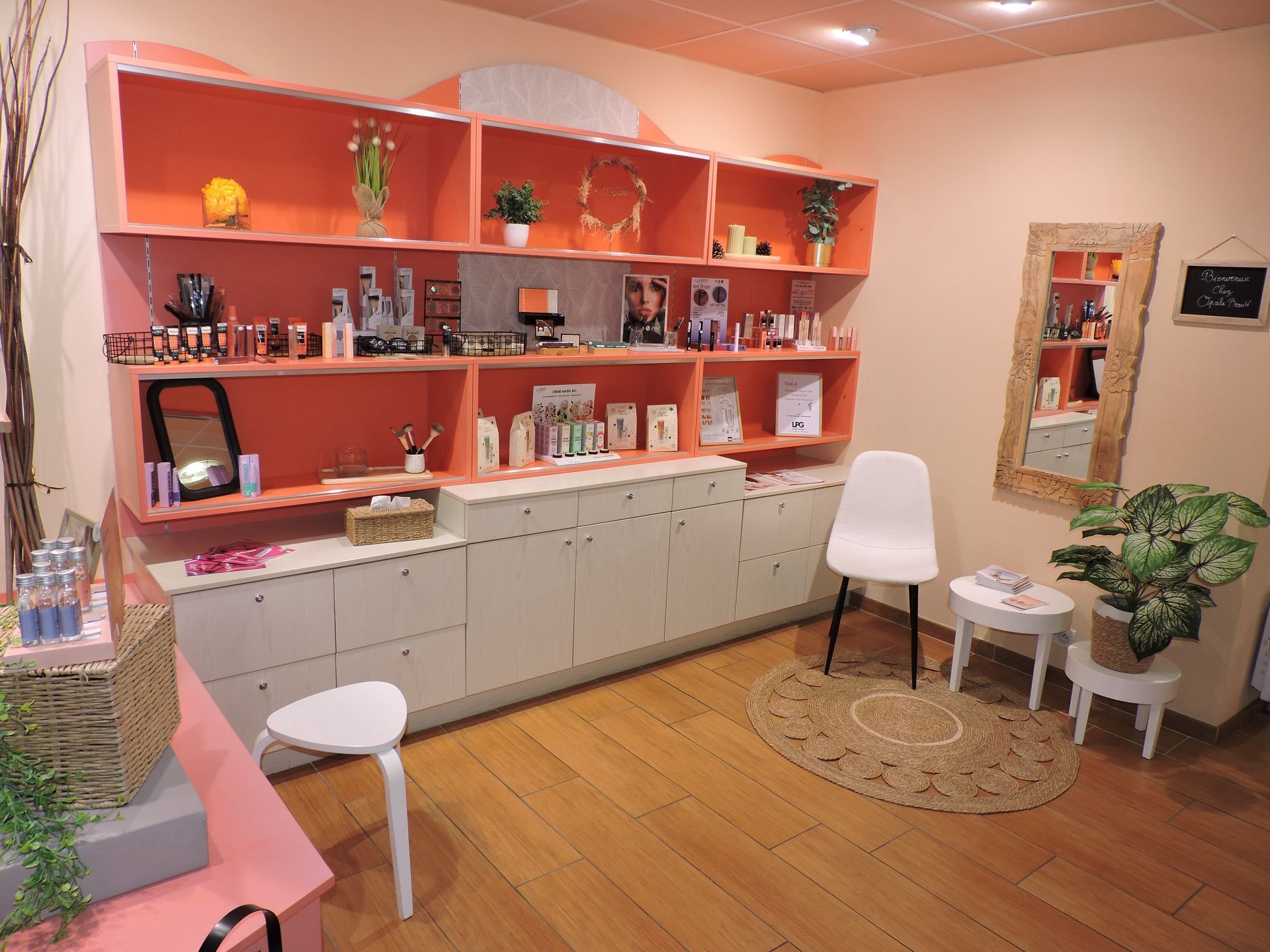 Intérieur d'un salon de beauté. Des étagères présentent les produits ; un petit coin salon avec des plantes et un miroir.