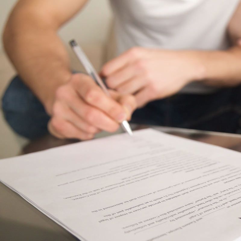 Persona firmando un documento con un bolígrafo en una mesa.