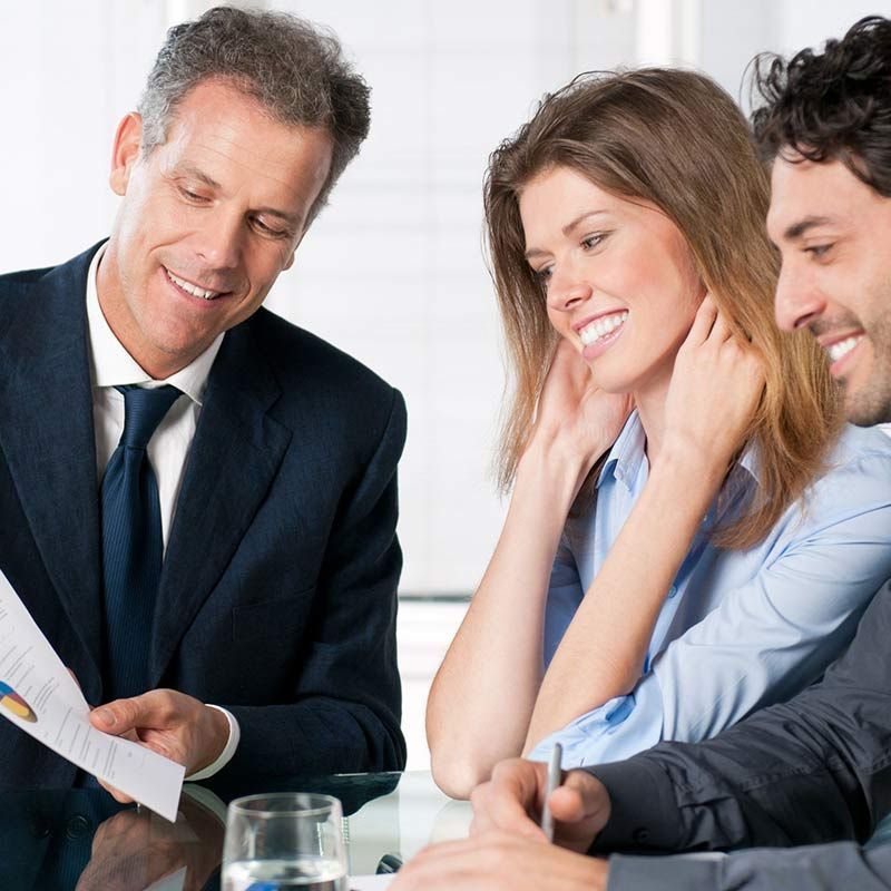 Tres compañeros de trabajo en una reunión, sonriendo y revisando documentos en una mesa.