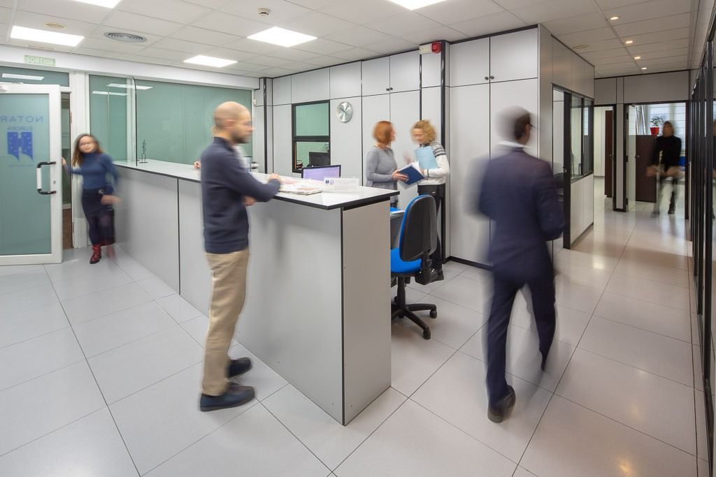 Gente en el vestíbulo o la recepción de una oficina moderna; un hombre atiende un mostrador y otros caminan cerca.