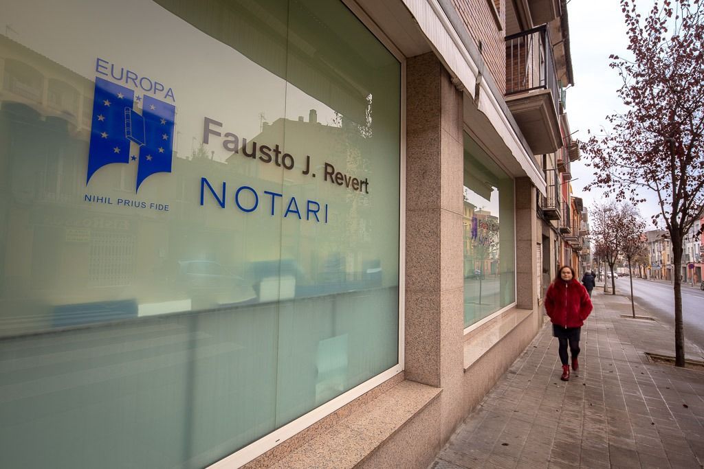 Vista de la calle de una notaría con ventanas esmeriladas y una persona caminando por la acera.