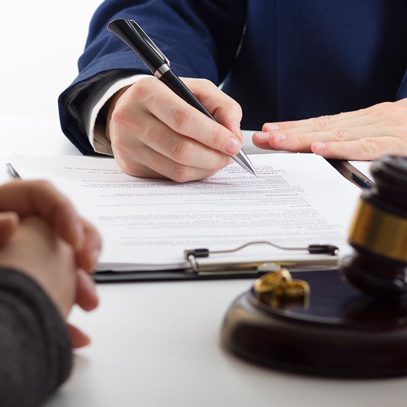 Abogado firmando documentos legales en un escritorio con un mazo en primer plano.