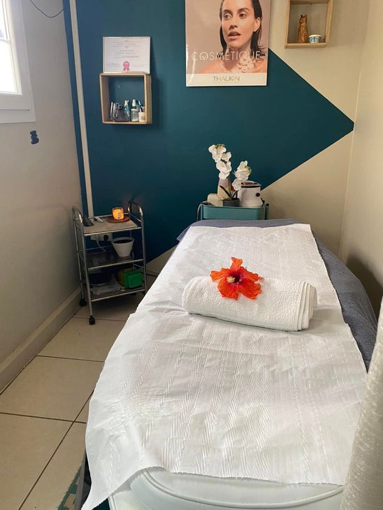 Salle de soins spa avec table de massage, draps blancs, mur turquoise et décoration florale