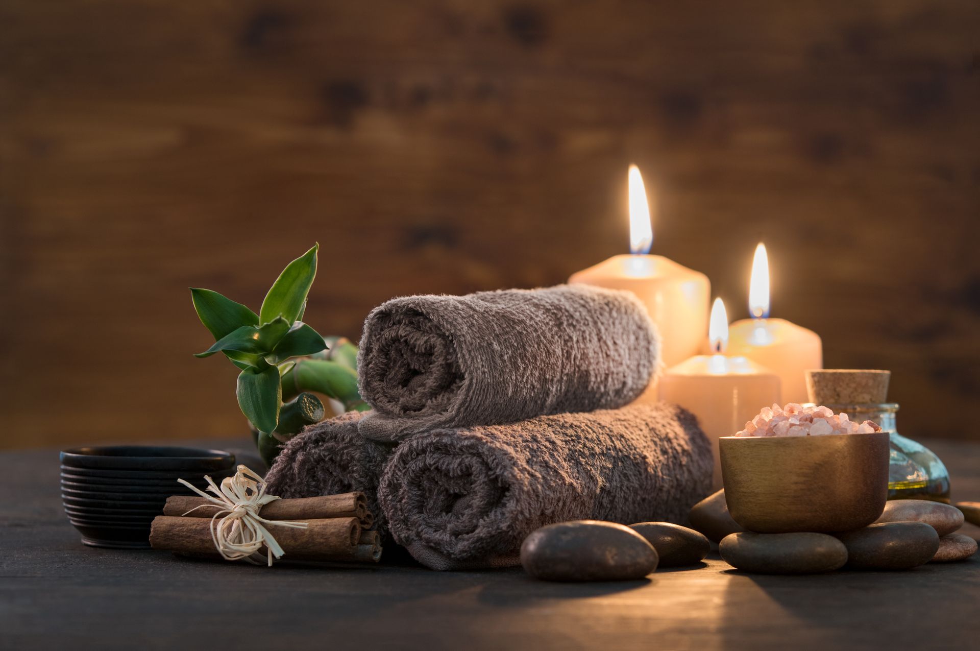 Bougies de spa, serviettes brunes roulées, pierres empilées et feuilles vertes sur une table en bois