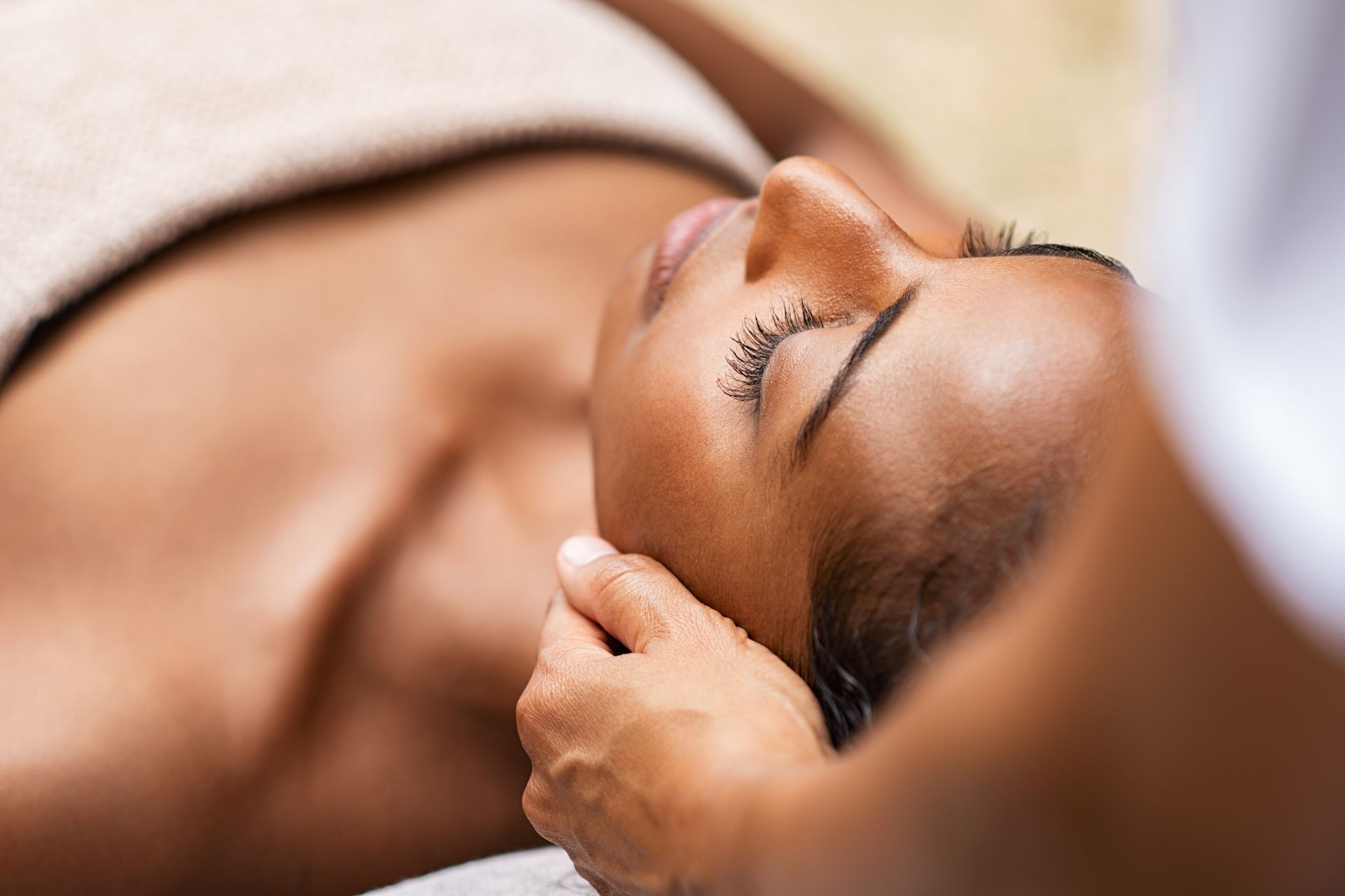 Une personne recevant un massage facial les yeux fermés dans un spa