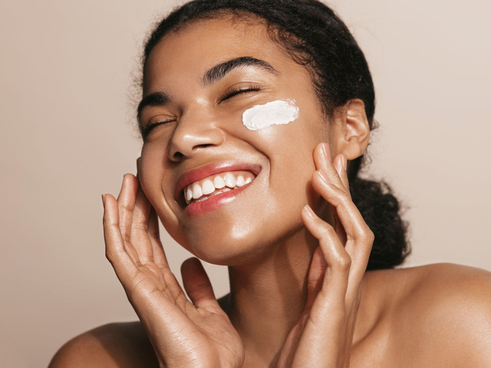 Personne souriante appliquant de la crème blanche sur les joues.