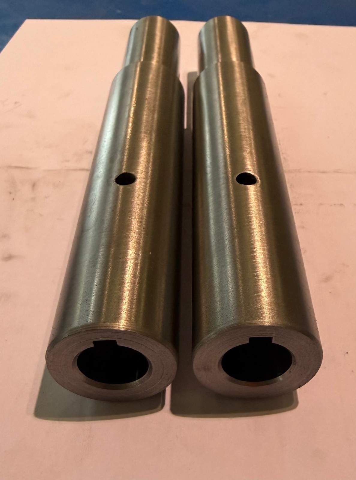 Dos piezas cilíndricas de metal plateado con orificios laterales, colocadas en posición vertical sobre una superficie plana.
