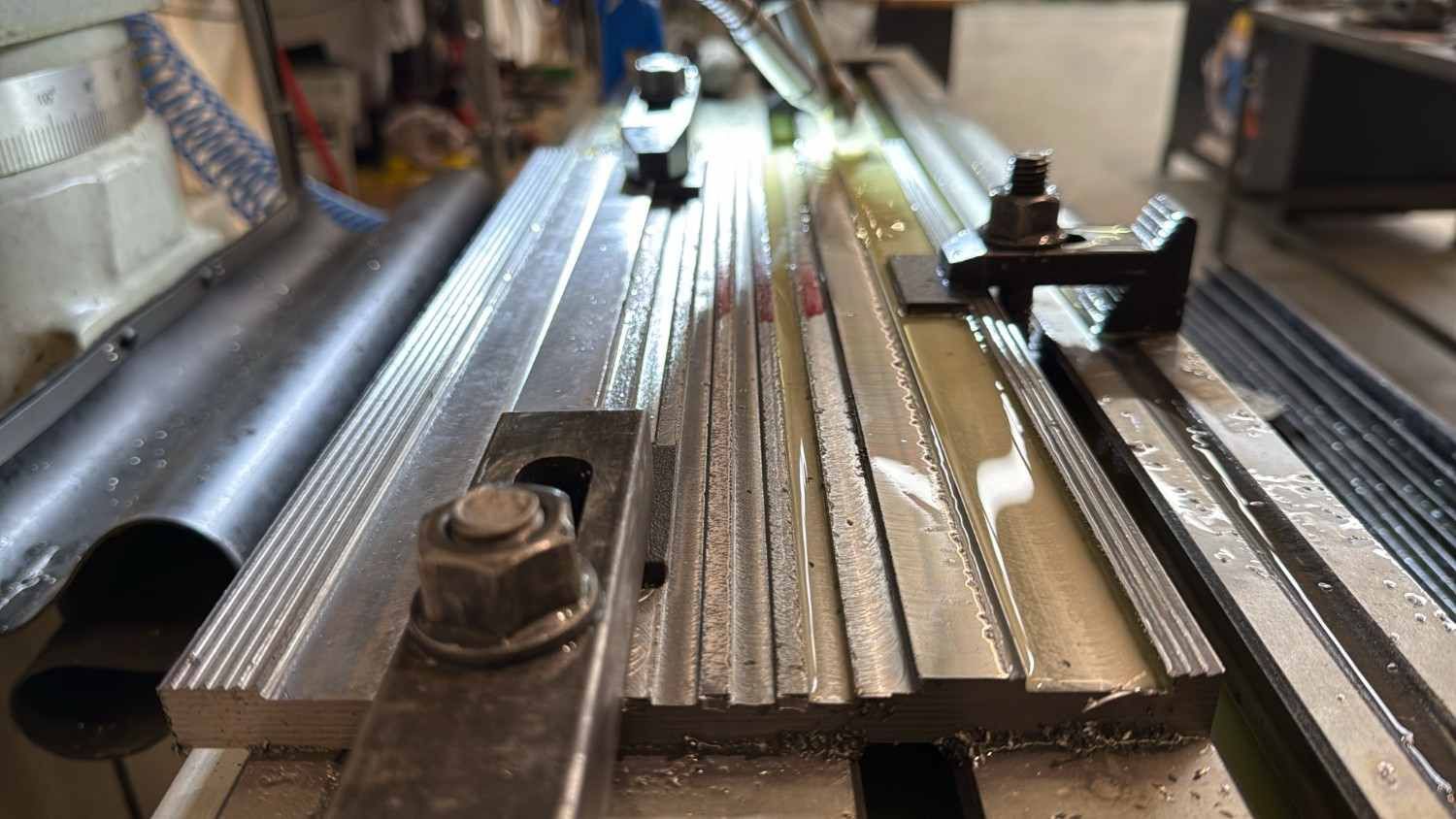 Primer plano de unos rieles y soportes metálicos sobre un banco de trabajo, con un pequeño gato blanco y negro al fondo.