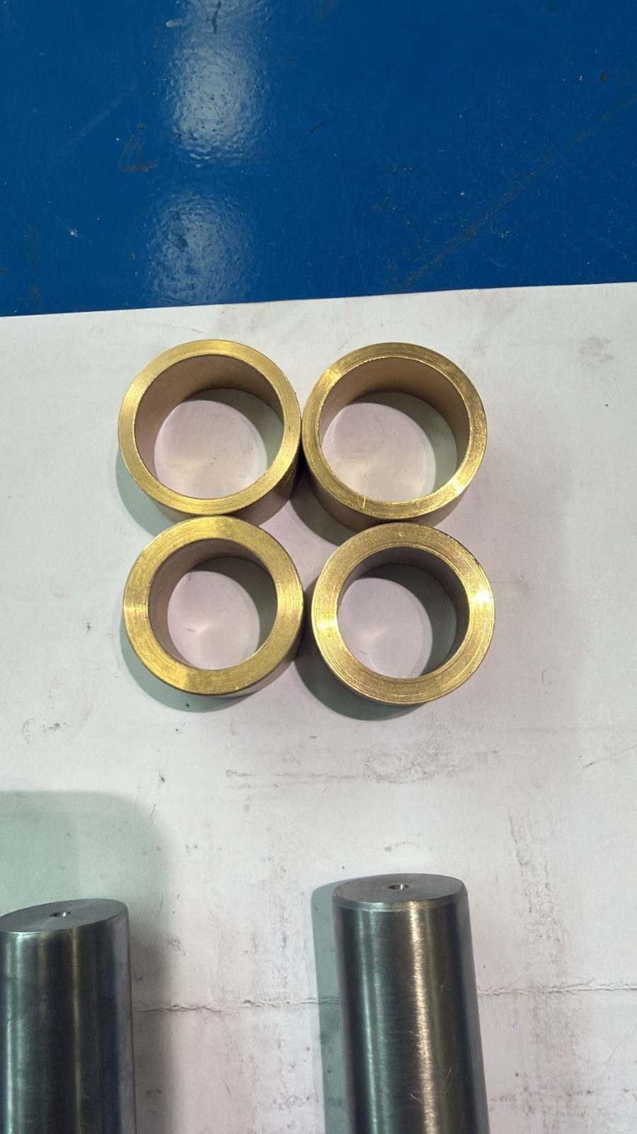 Cuatro anillos de latón dispuestos en forma de cuadrado sobre una superficie blanca, con dos cilindros metálicos.