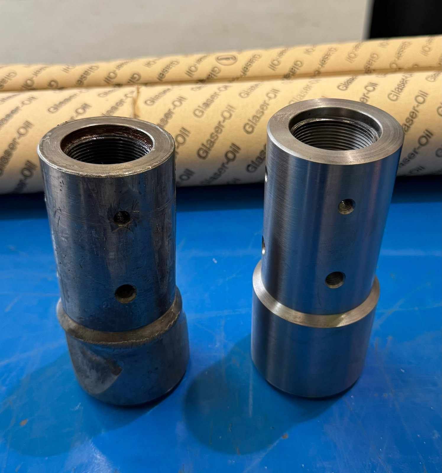 Dos piezas cilíndricas de metal con la parte superior roscada, una oscura y otra plateada, de pie sobre una superficie azul.