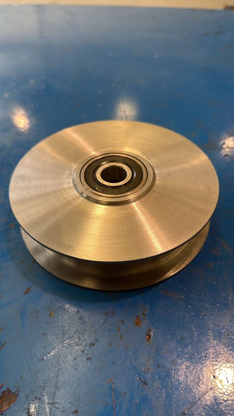 Pequeña rueda o polea de metal con un rodamiento, sobre un banco de trabajo azul.