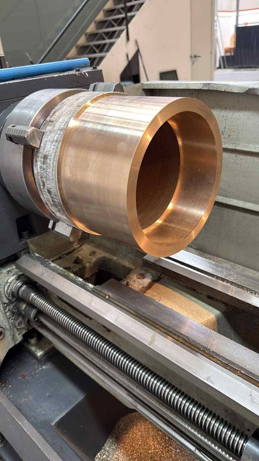 Tubo de metal cobrizo mecanizándose en un torno en un taller industrial.