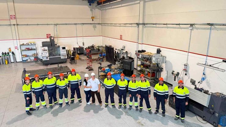 Grupo de trabajadores con chalecos de alta visibilidad posando en un taller, con equipos y herramientas detrás