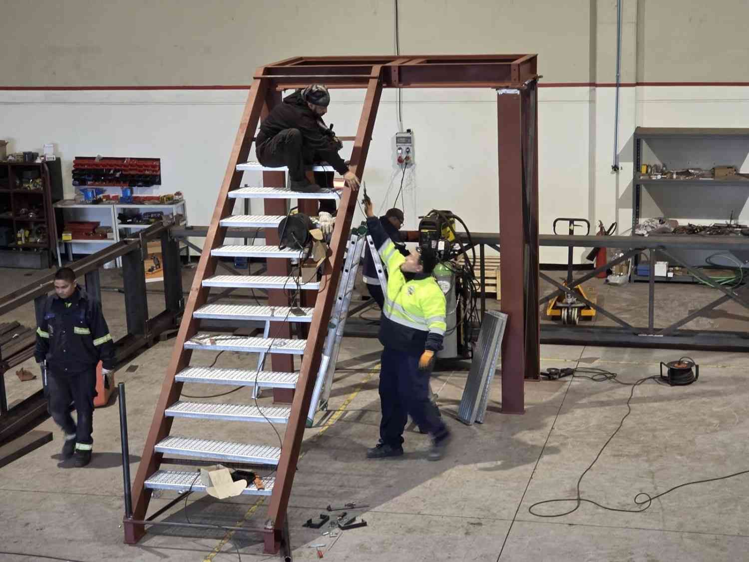 Trabajadores subiendo por una plataforma con escaleras metálicas en un taller.