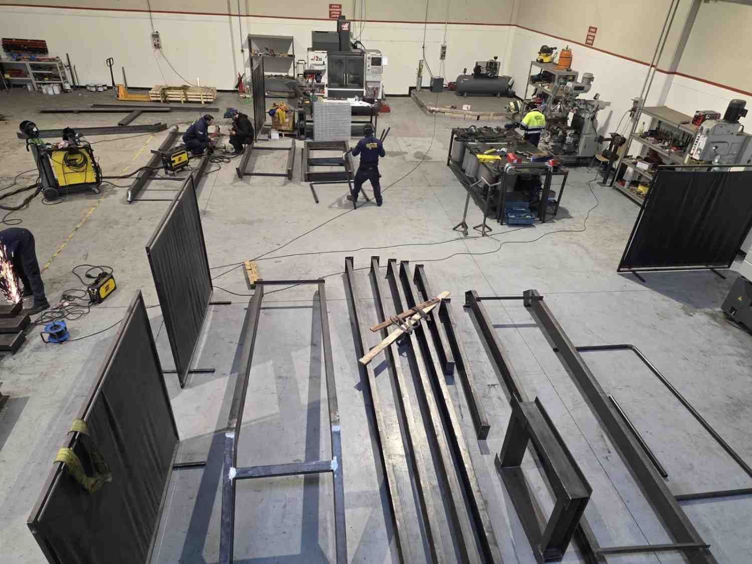 Taller industrial donde los trabajadores montan grandes estructuras metálicas y equipos en el suelo