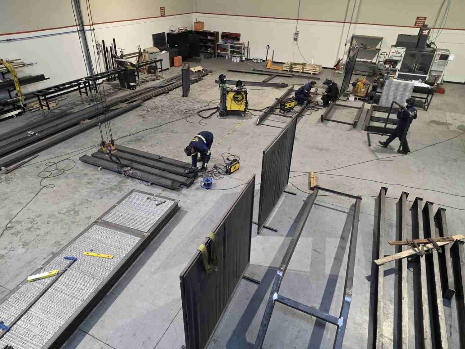 Trabajadores instalando grandes paneles metálicos en un taller industrial, rodeados de herramientas y equipos
