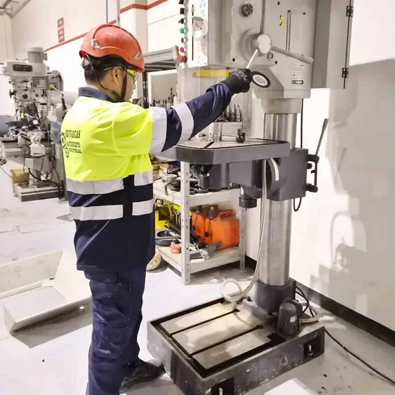 Hombre con equipo de seguridad operando un taladro de columna en un taller.
