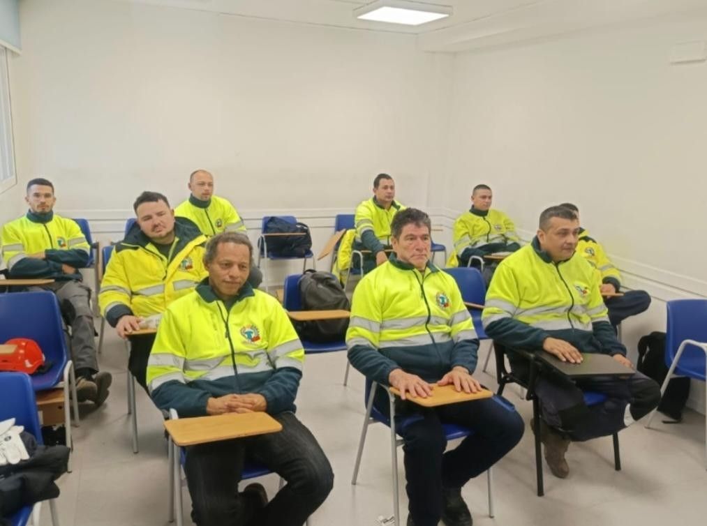 Personas con chaquetas amarillo neón sentadas en un aula, escuchando atentamente.