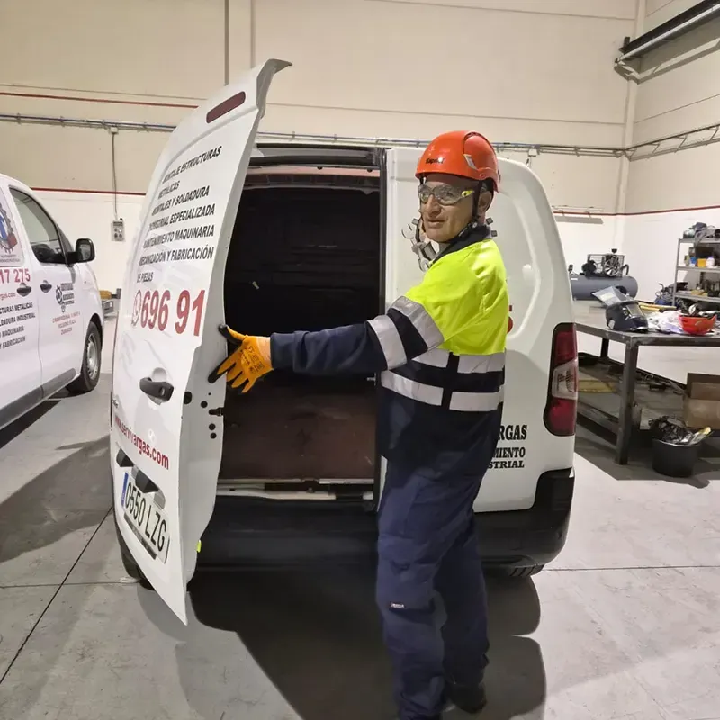 Hombre con equipo de seguridad abriendo la puerta de una camioneta blanca dentro de un garaje.