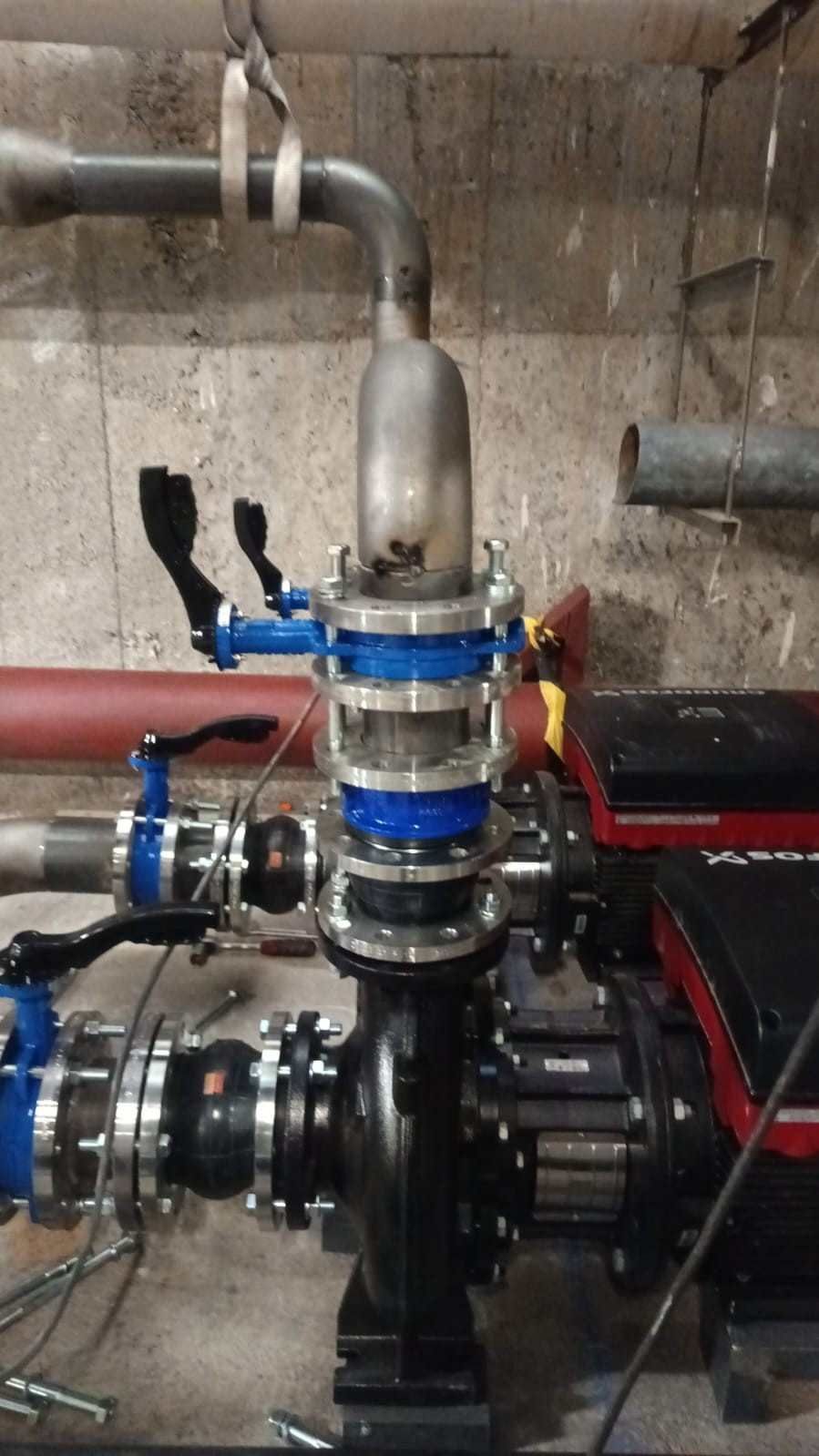 Tuberías industriales y conjunto de bomba con abrazaderas azules, tubos rojos y un motor.