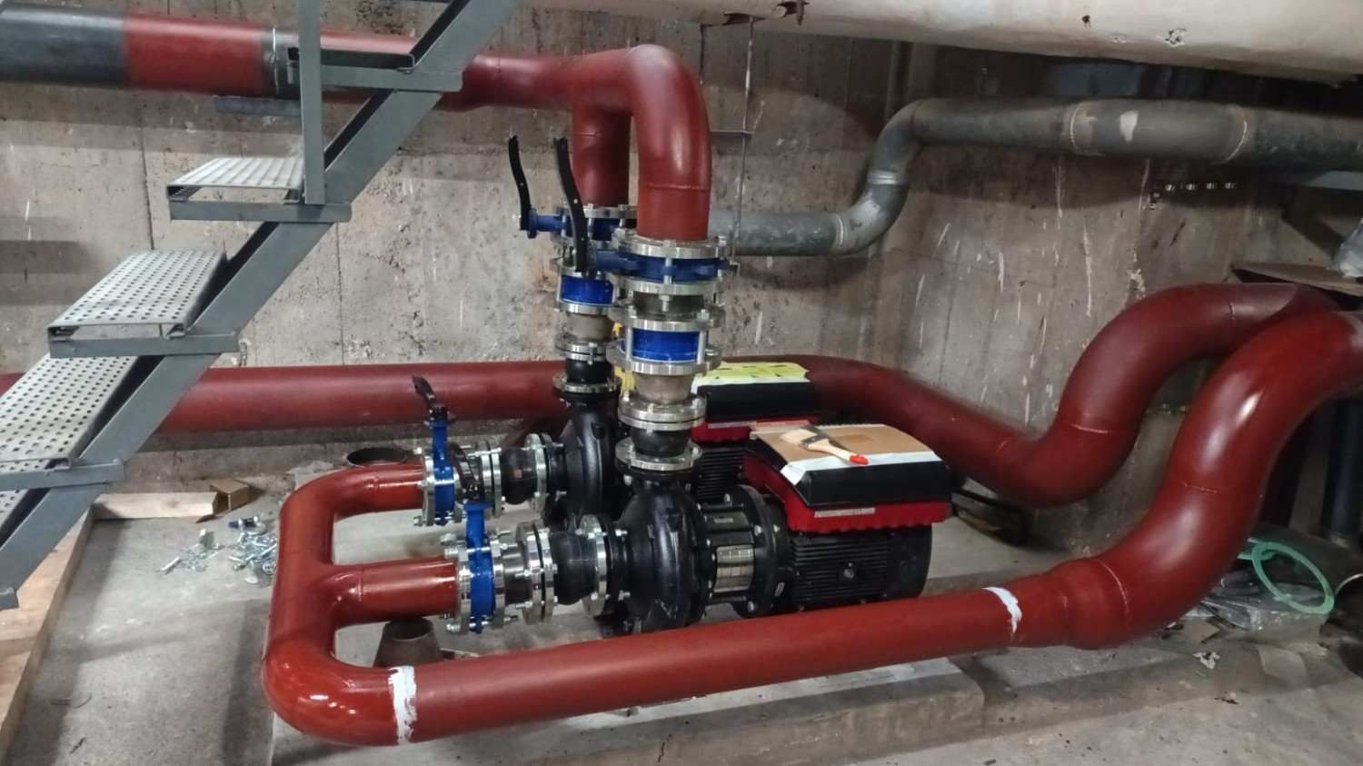 Tuberías industriales rojas con aislamiento, conectadas a un conjunto de bombeo en una sala de máquinas.