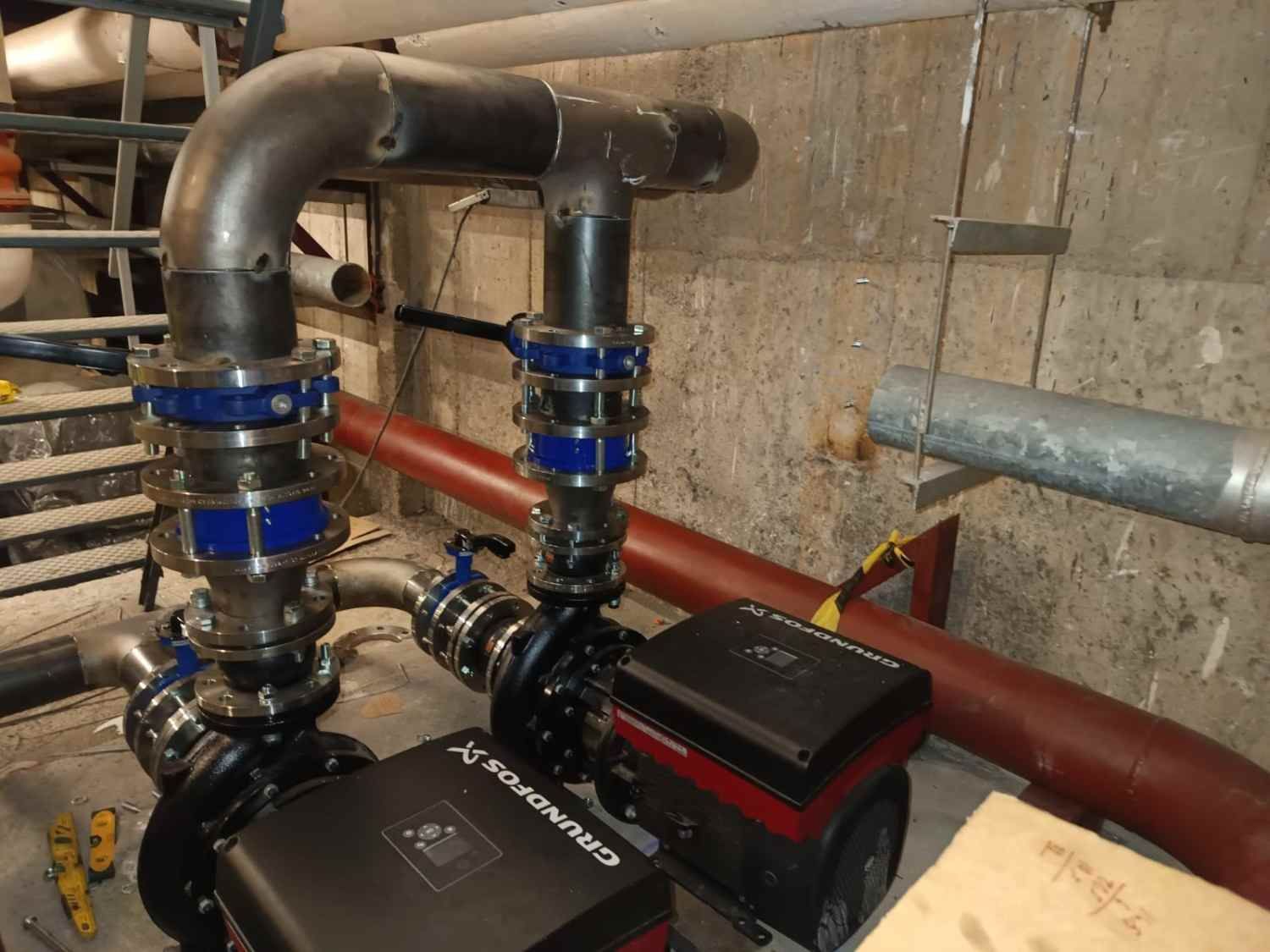 Dos bombas negras con acoplamientos azules conectadas a tuberías grises en una sala de máquinas