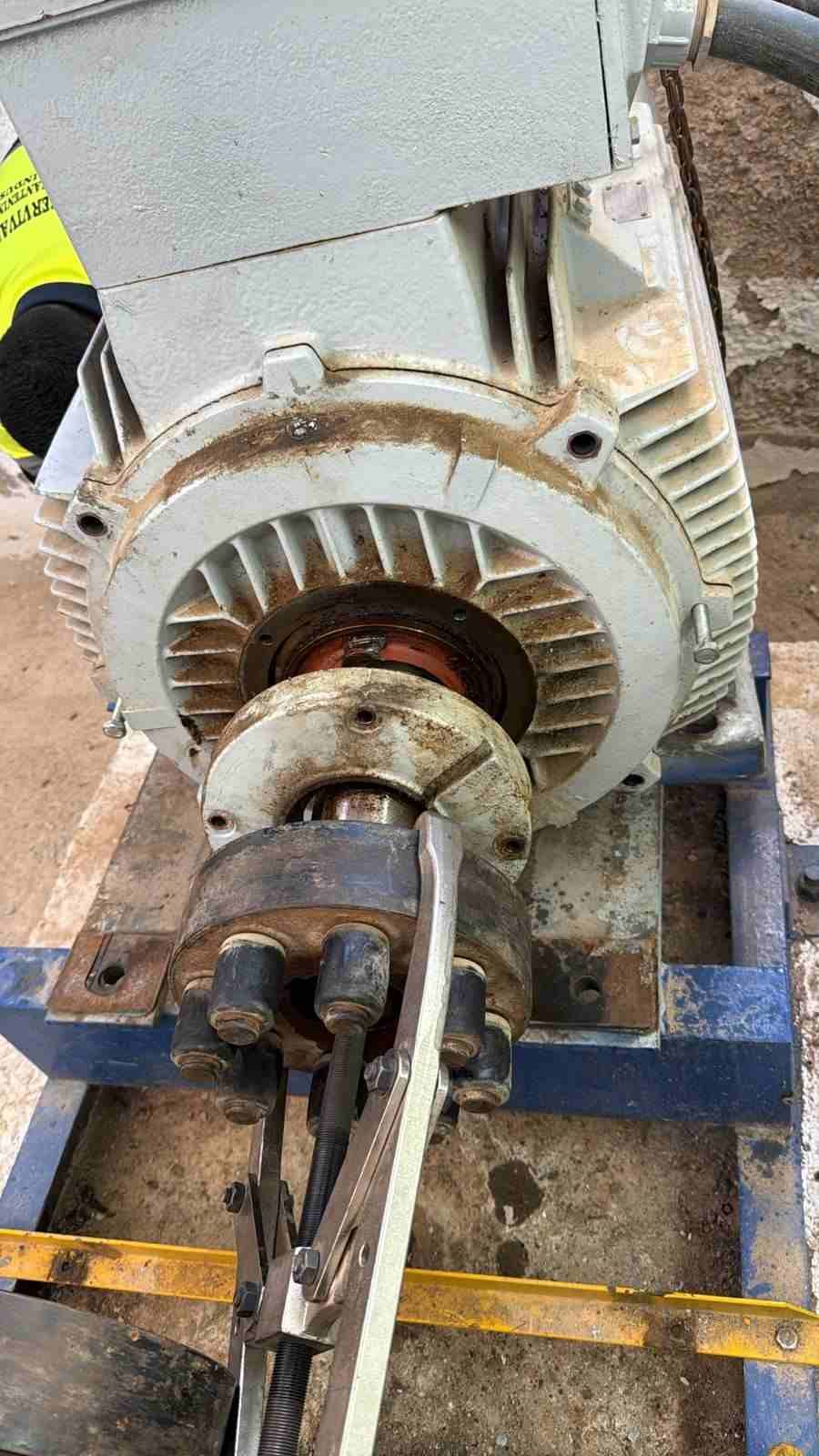 Motor eléctrico industrial montado sobre un bastidor azul, con un acoplamiento de eje visible en un taller