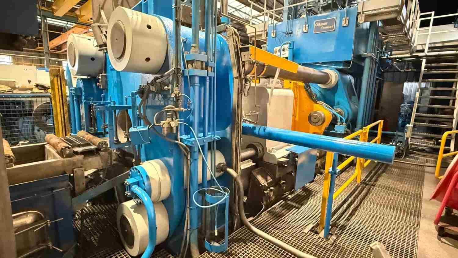 Máquina industrial azul con tuberías y rodillos en el interior de un taller fabril