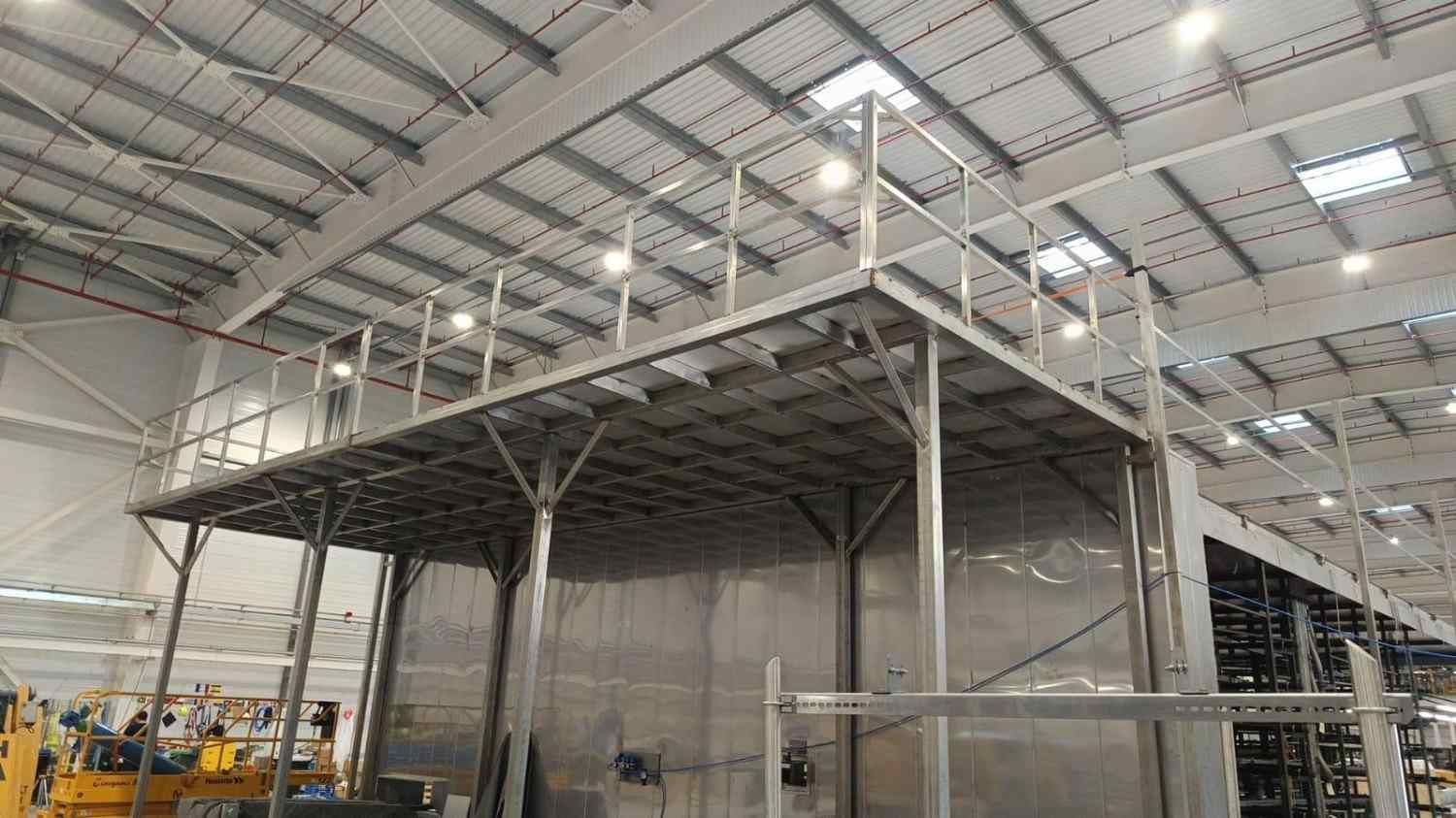 Interior de una gran nave industrial, con una plataforma de entreplanta de acero y luminarias en un techo alto