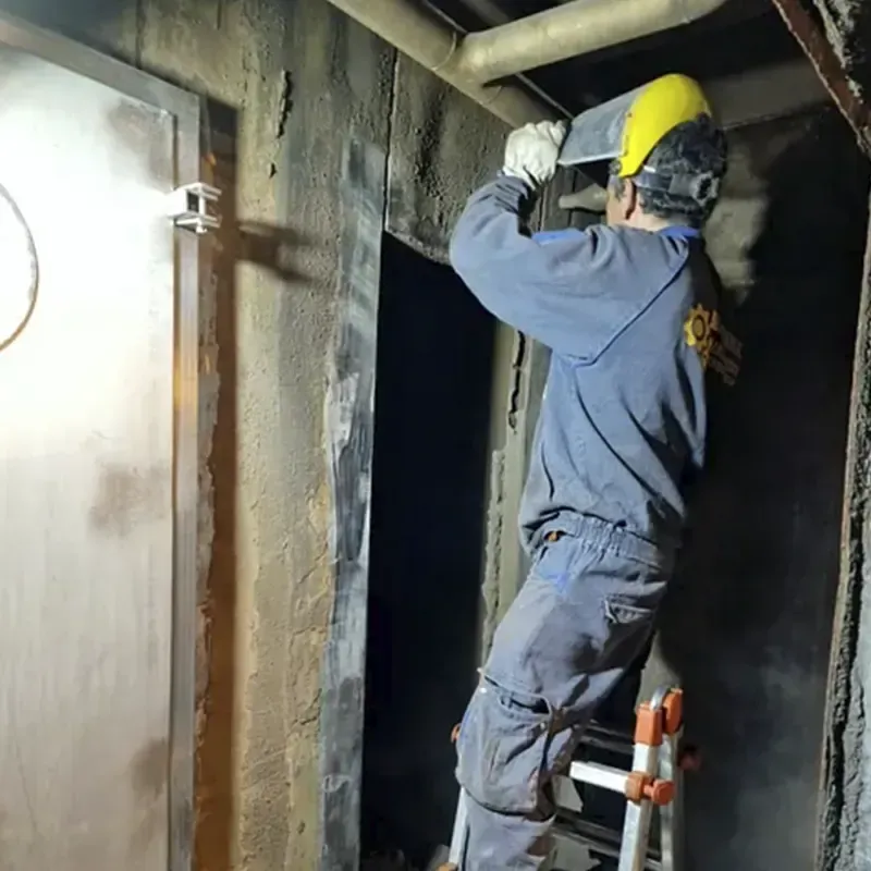Trabajador en una escalera instalando o reparando algo en una habitación oscura y de hormigón.