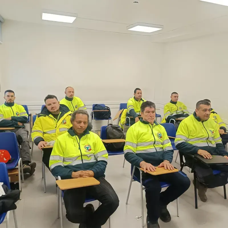 Aula con personas con chalecos salvavidas. Están sentados, mirando al frente, y algunos tienen computadoras portátiles.