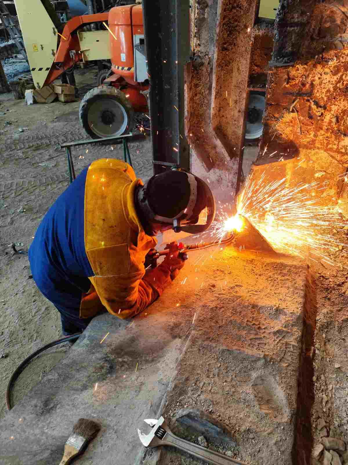 Un trabajador usa una amoladora sobre metal, creando brillantes chispas en una zona industrial.
