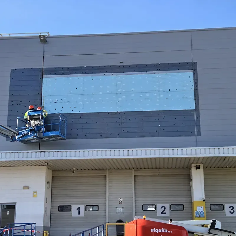 Trabajadores en un ascensor reparando la pared exterior de un almacén, esquema de colores gris y azul.