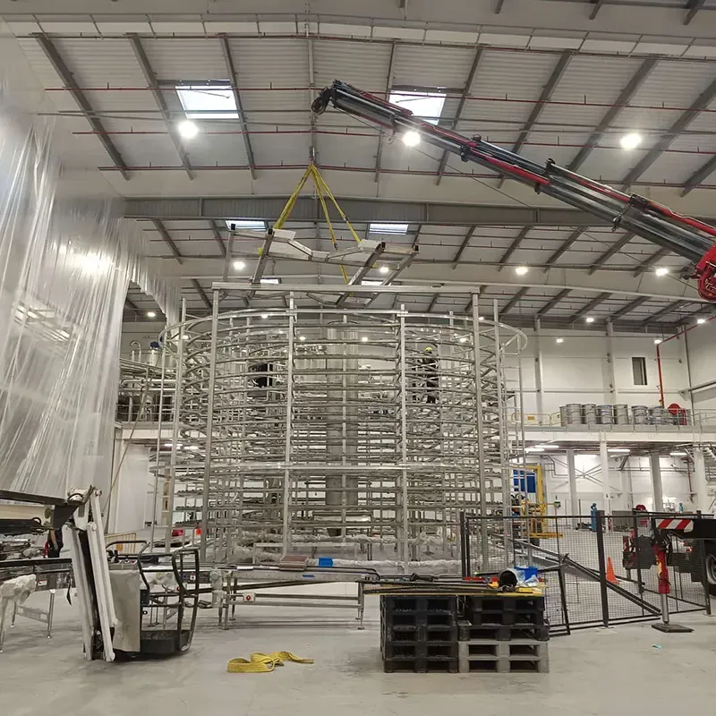 Una gran estructura metálica se monta en el interior de un almacén con una grúa encima, posiblemente para uso industrial.