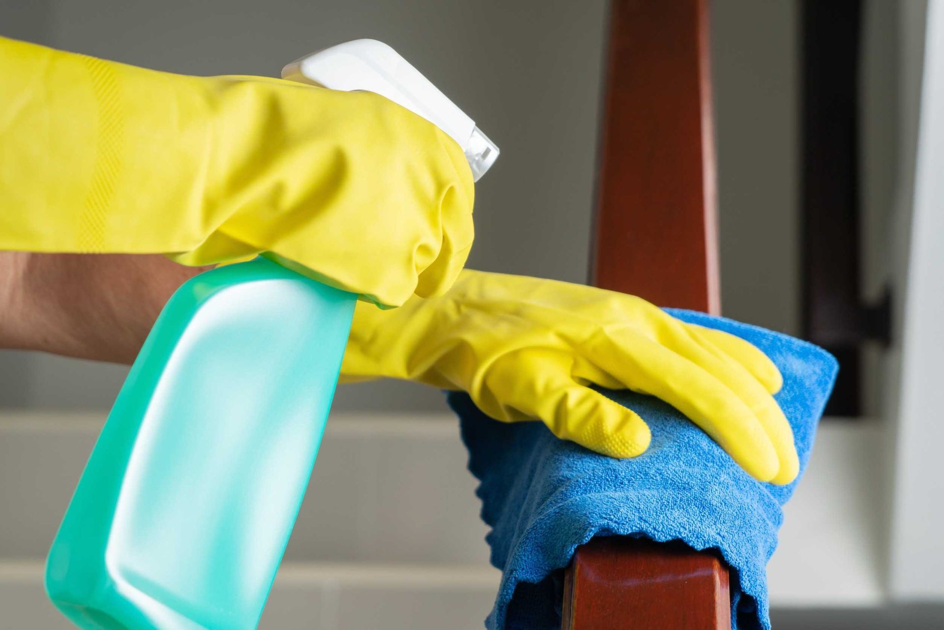 Una persona que lleva guantes amarillos está limpiando una silla con un paño y una botella de spray.