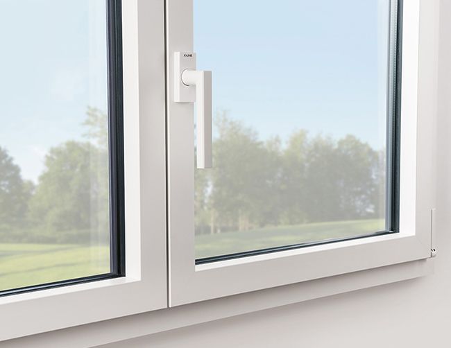 Fenêtre à battants blanche avec poignée ouverte, donnant sur un champ verdoyant et des arbres sous un ciel bleu.