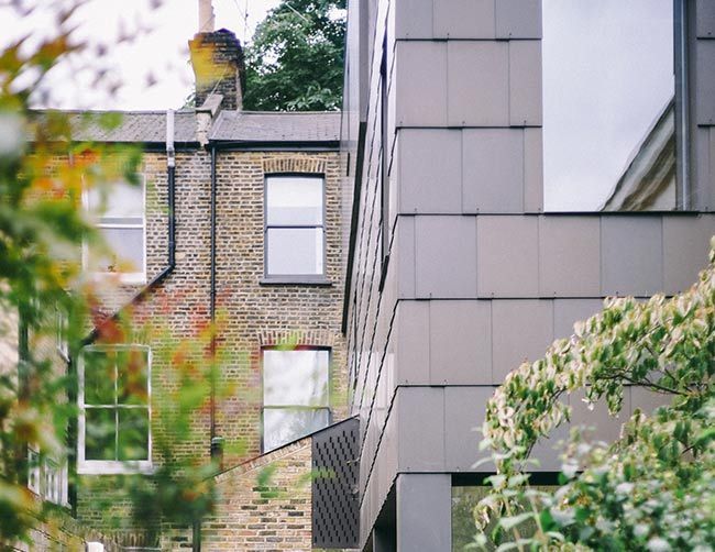 Bâtiment gris moderne à côté d'un vieux bâtiment en briques ; végétation au premier plan.