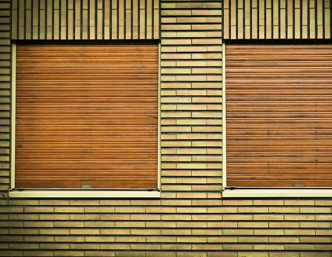 Deux fenêtres avec des volets roulants bruns fermés dans un mur de briques.