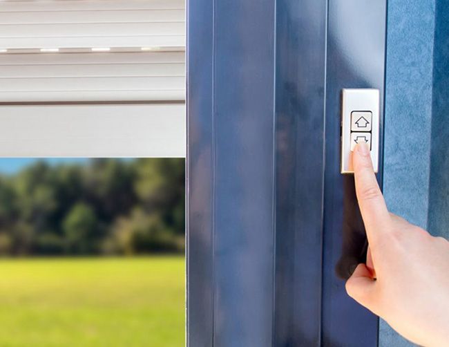 Une main appuie sur le bouton flèche vers le bas d'un interrupteur pour baisser un store, avec un champ vert visible.