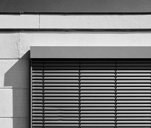 Stores vénitiens horizontaux gris sur le mur d'un bâtiment, projetant une ombre.