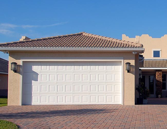 Porte de garage blanche sur une maison beige avec une allée en briques sous un ciel bleu.