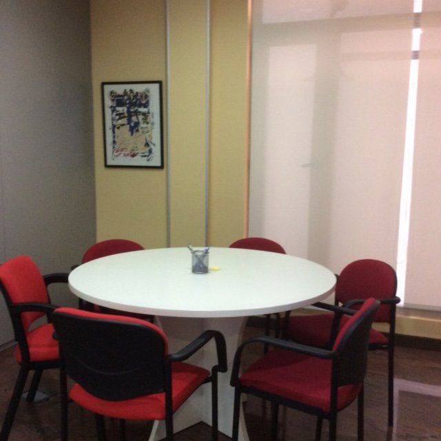 Una mesa redonda con sillas rojas y un cuadro en la pared encima.