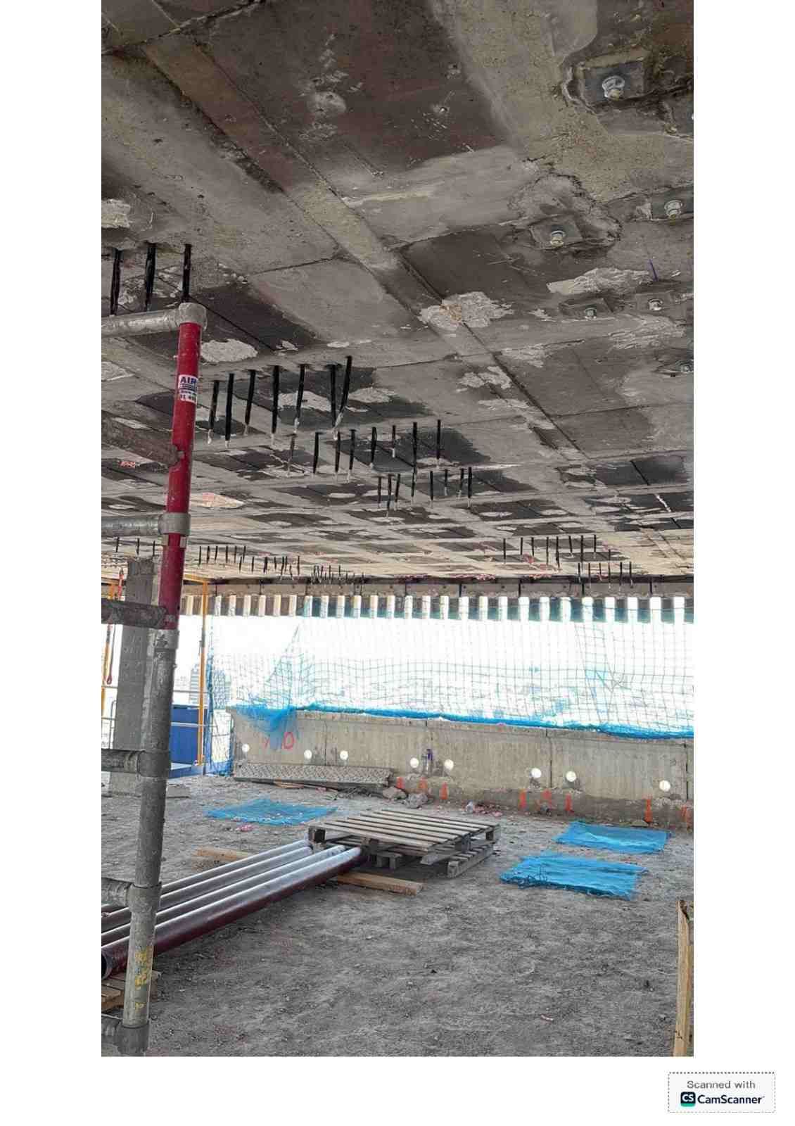 Obra en construcción con techo de hormigón sin terminar, andamios y materiales apilados sobre un suelo de grava