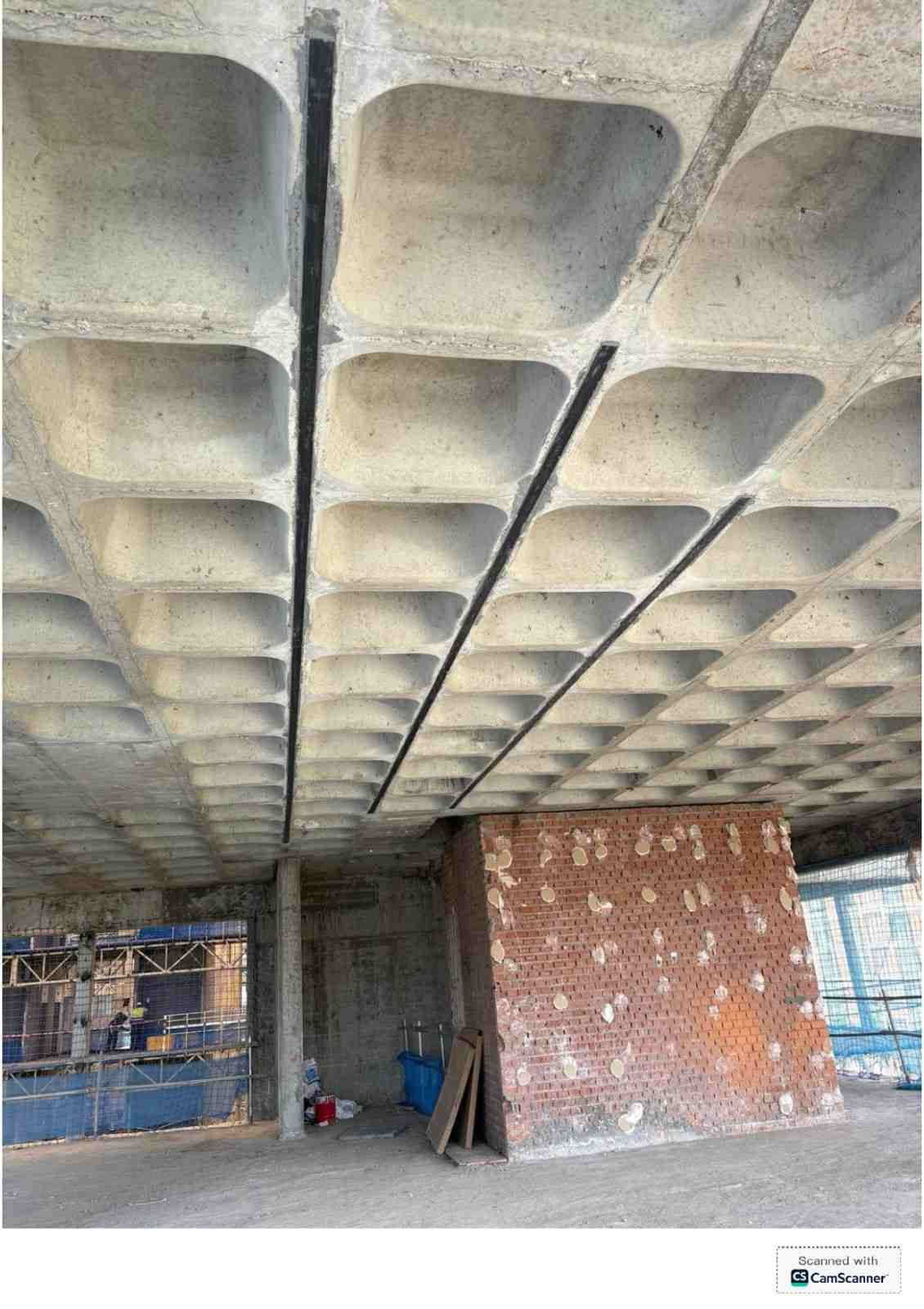 Parte inferior de un techo de hormigón en construcción, con una pared de ladrillo y andamios debajo.